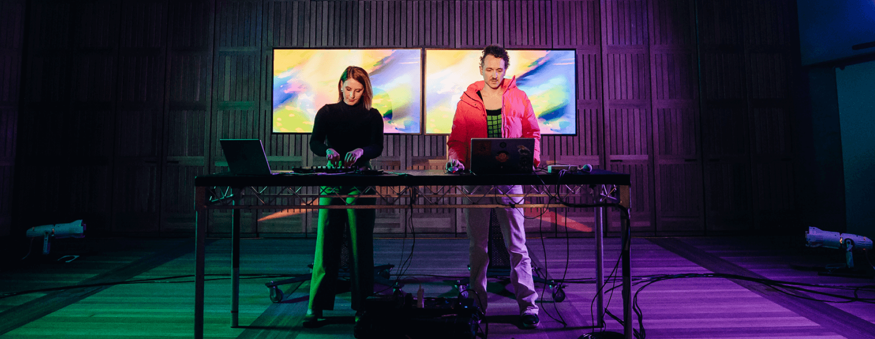 Two performers standing in front of a colorful stage ready to play music